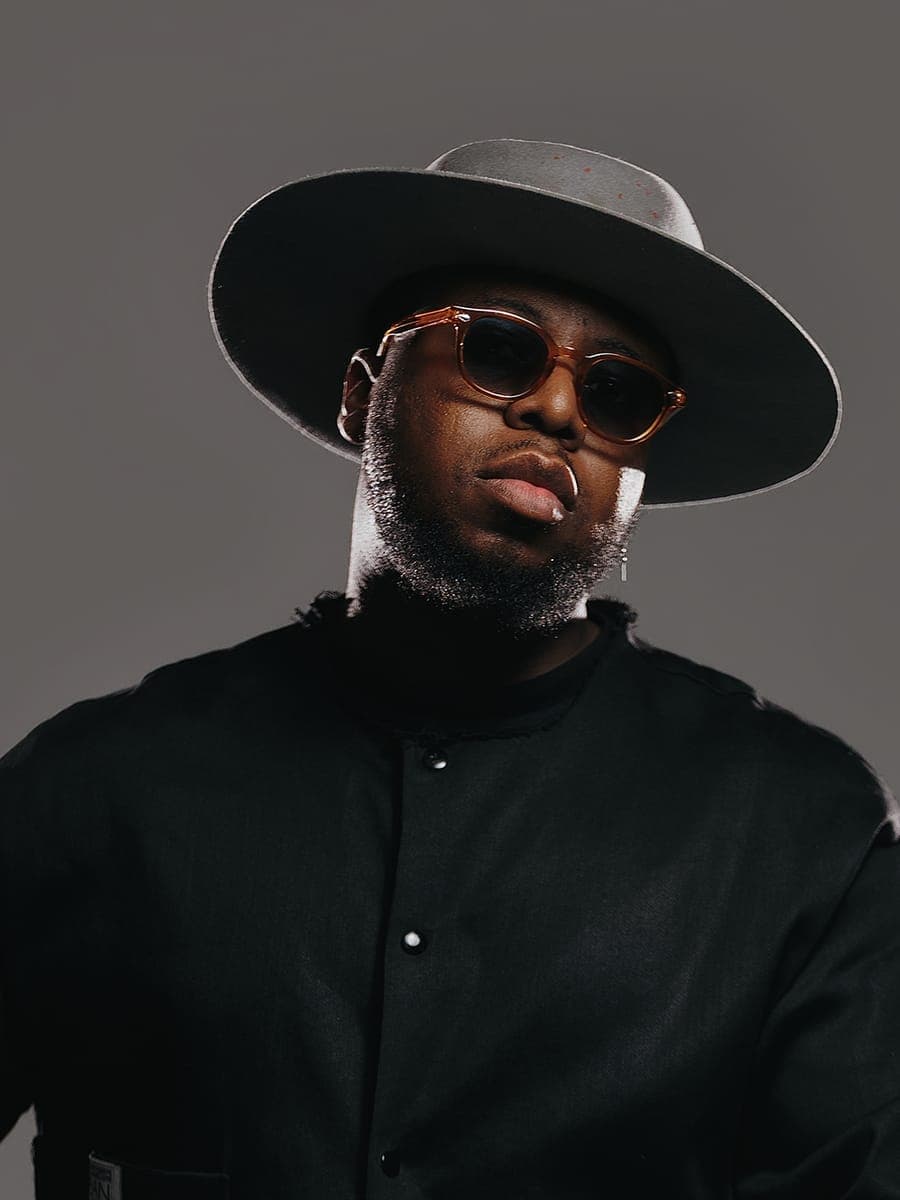 JOĒHUMAN in a wide-brimmed hat and tinted glasses, looking into the camera