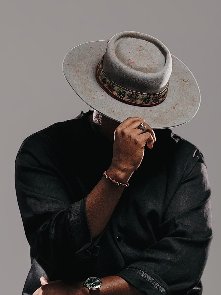 JOĒHUMAN holding the brim of a patterned hat over his face